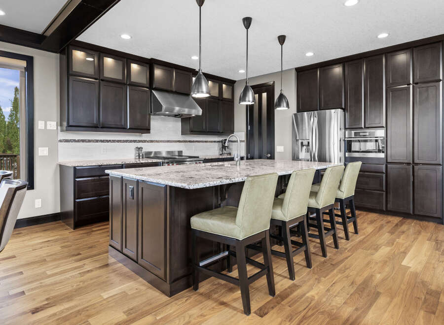 Experience luxury in this stunning kitchen featuring dark wood cabinetry, a large granite island with bar seating, and top-of-the-line stainless steel appliances.