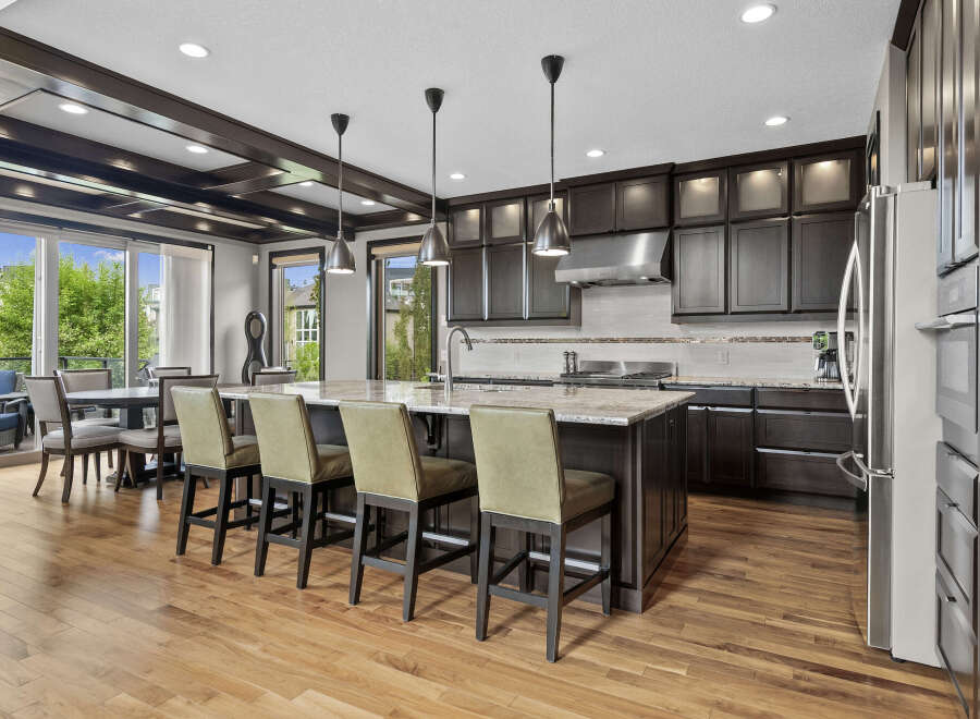 Experience luxury in this stunning kitchen, featuring dark wood cabinetry, a spacious granite island with bar seating, and a professional-grade stainless steel range hood.