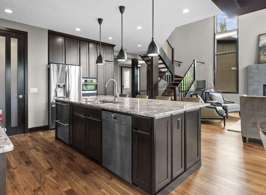 Experience luxury in this modern kitchen featuring a large granite island with a double sink and stainless steel appliances.