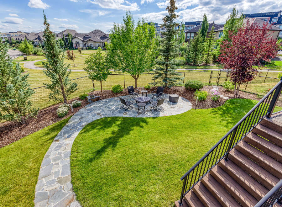 Enjoy outdoor living in this beautifully landscaped backyard featuring a stone patio with a fire pit and seating area, perfect for gatherings.