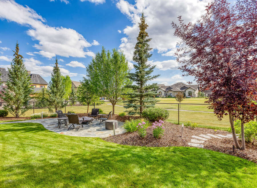 Enjoy outdoor living in this beautifully landscaped backyard featuring a spacious stone patio with comfortable seating and a fire pit, perfect for gatherings.