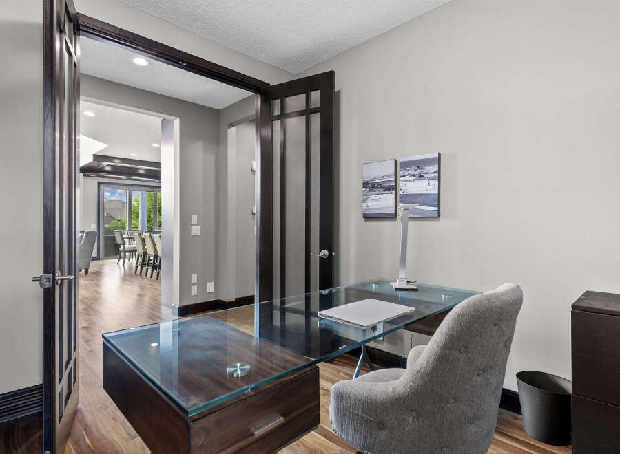 Step into this elegant home office, featuring a sleek glass-top desk with a dark wood base, complemented by a comfortable upholstered chair.