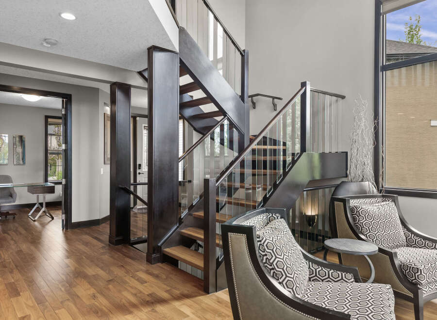 Experience modern luxury in this stunning home featuring a dramatic open-riser staircase with glass railings and dark wood accents.