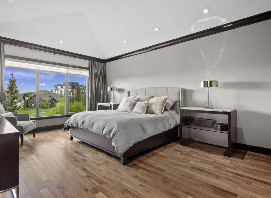 Experience luxury in this spacious master bedroom featuring a king-sized bed with a plush upholstered headboard and elegant decorative pillows.