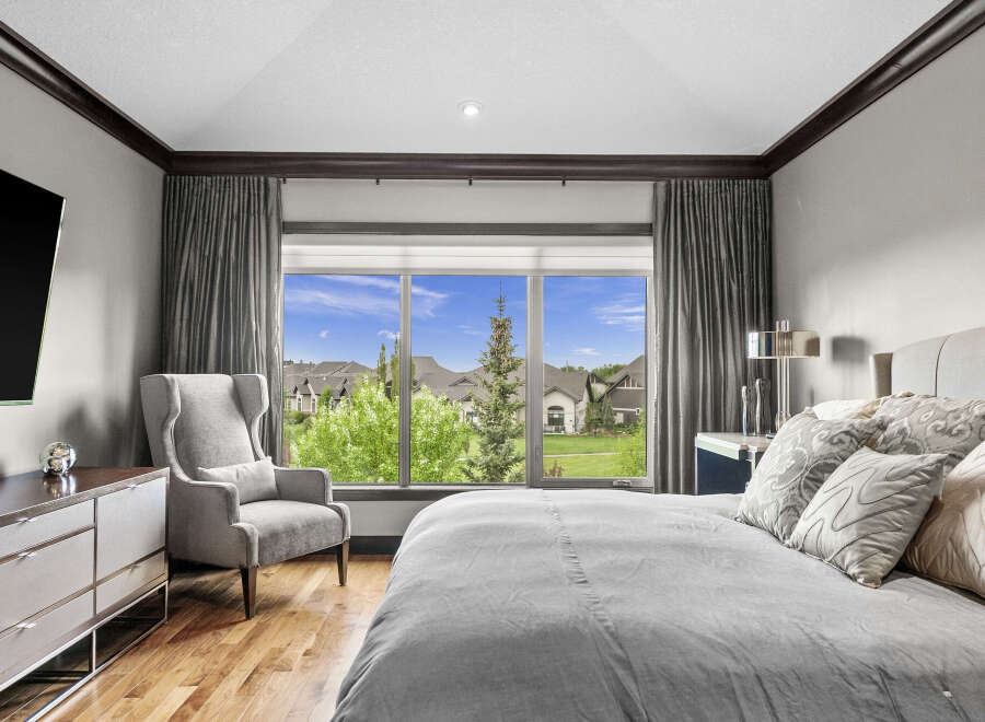 Experience luxury living in this stunning bedroom featuring a large window with picturesque views of the neighborhood and lush greenery.