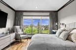 Experience luxury living in this stunning bedroom featuring a large window with picturesque views of the neighborhood and lush greenery.