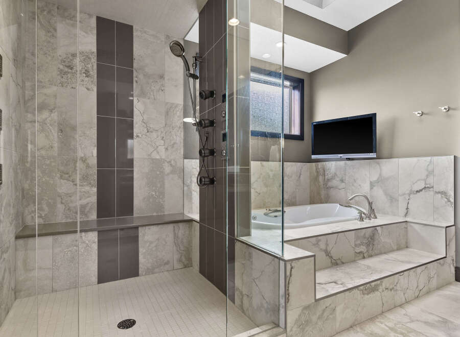 Experience ultimate relaxation in this luxurious master bathroom, featuring a spacious walk-in shower with multiple shower heads and a built-in bench.