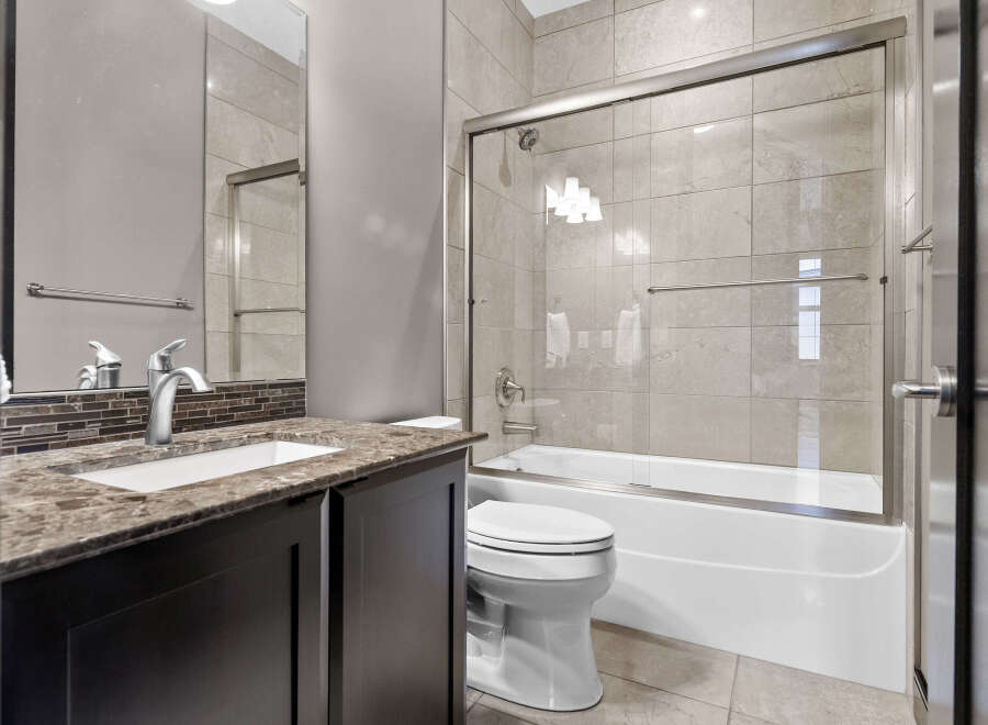 This modern bathroom features a sleek vanity with a granite countertop and a stylish mosaic backsplash.