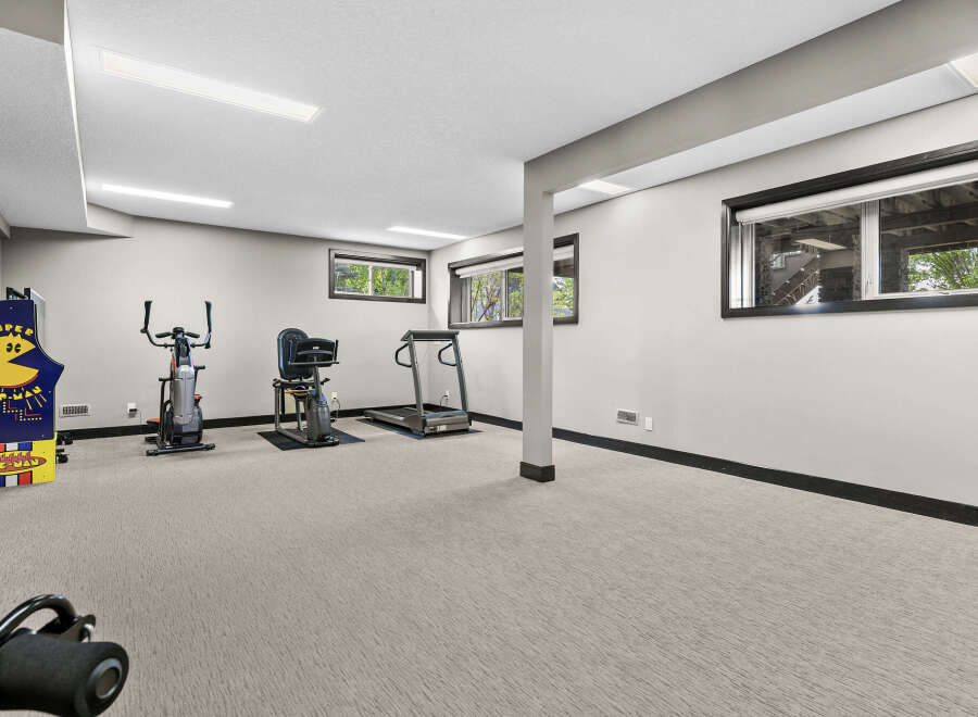 This finished basement offers a dedicated home gym space, complete with a treadmill, stationary bike, and a vintage arcade game.