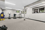This finished basement offers a dedicated home gym space, complete with a treadmill, stationary bike, and a vintage arcade game.