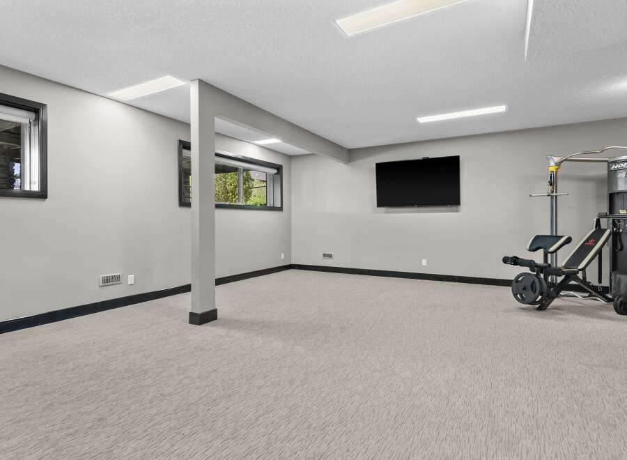 Transform this versatile basement space into your personal home gym, complete with a mounted flat-screen TV for entertainment and a multi-functional weight machine.