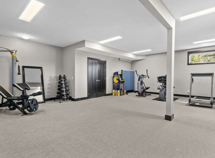 Transform this spacious basement into your ultimate home gym, complete with a versatile weight bench, a full rack of dumbbells, and multiple cardio machines like a treadmill and stationary bikes.