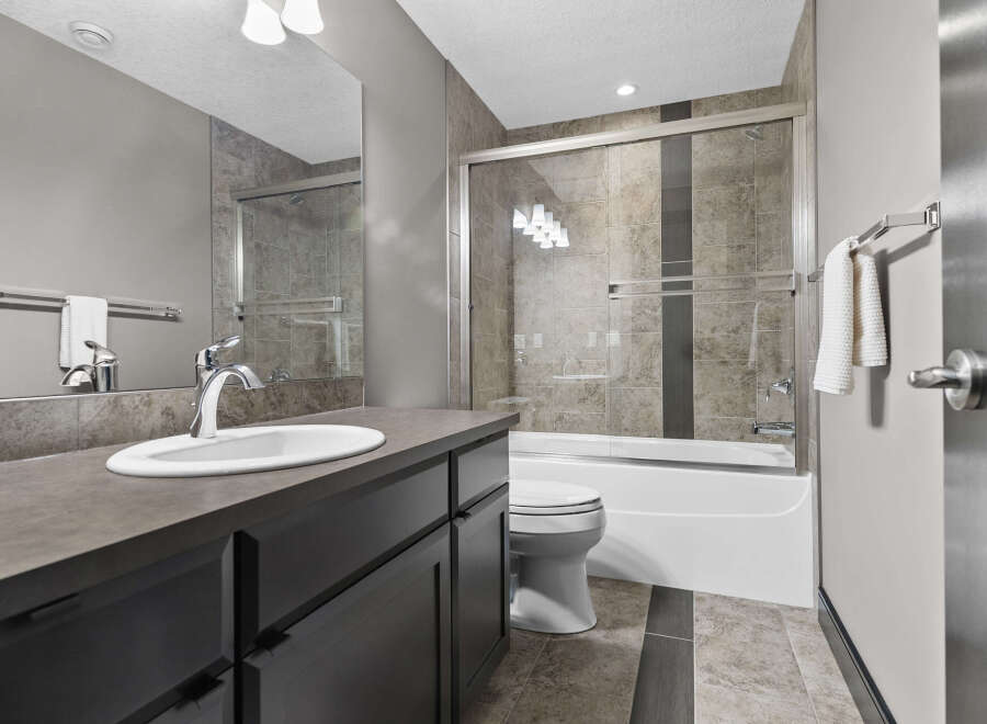 This modern bathroom features a sleek vanity with a white undermount sink and a chrome faucet, complemented by a large mirror.