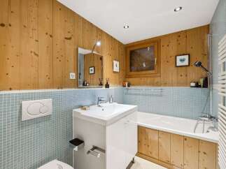 Experience rustic charm in this bathroom featuring warm, natural wood paneling and a soothing light blue tiled wainscoting.