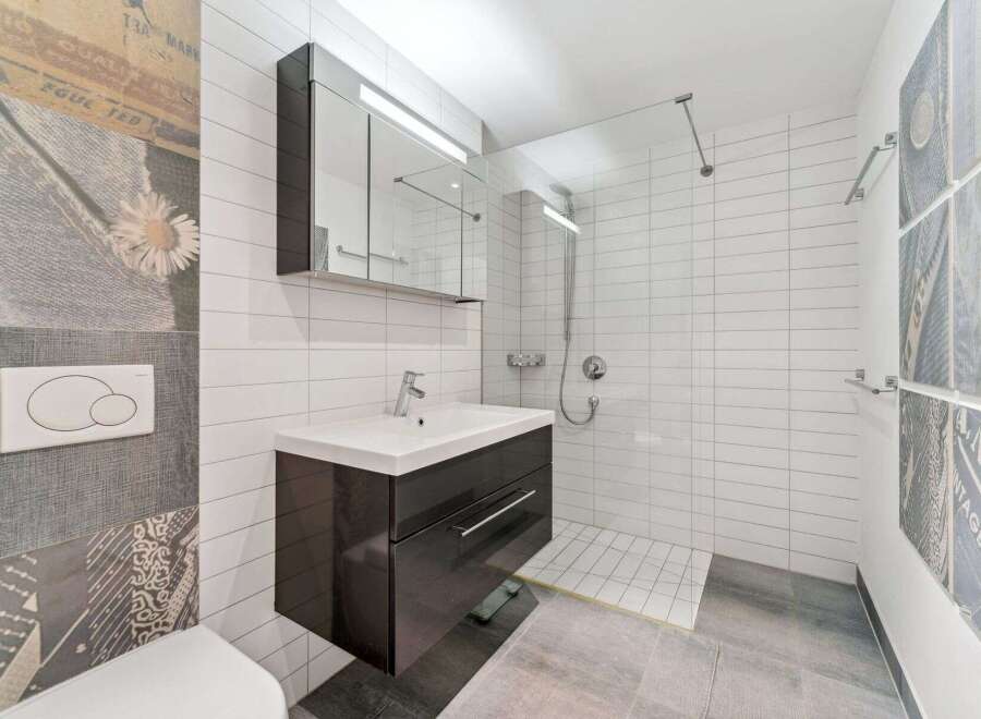This modern bathroom features a sleek vanity with a white countertop and a dark cabinet, complemented by a large mirrored medicine cabinet with integrated lighting.