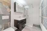This modern bathroom features a sleek vanity with a white countertop and a dark cabinet, complemented by a large mirrored medicine cabinet with integrated lighting.