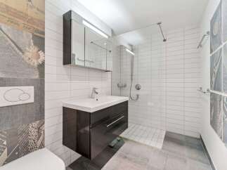 This modern bathroom features a sleek vanity with a white countertop and a dark cabinet, complemented by a large mirrored medicine cabinet with integrated lighting.