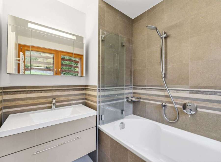 This modern bathroom features a sleek vanity with a white basin and ample storage, complemented by a large mirrored cabinet with integrated lighting.