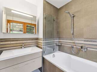 This modern bathroom features a sleek vanity with a white basin and ample storage, complemented by a large mirrored cabinet with integrated lighting.