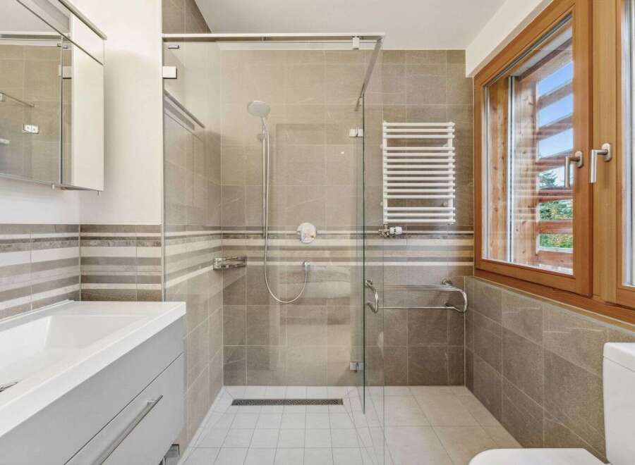 Experience modern comfort in this beautifully appointed bathroom, featuring a spacious glass-enclosed shower with a rainfall showerhead and a convenient heated towel rack.