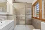 Experience modern comfort in this beautifully appointed bathroom, featuring a spacious glass-enclosed shower with a rainfall showerhead and a convenient heated towel rack.