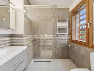 Experience modern comfort in this beautifully appointed bathroom, featuring a spacious glass-enclosed shower with a rainfall showerhead and a convenient heated towel rack.