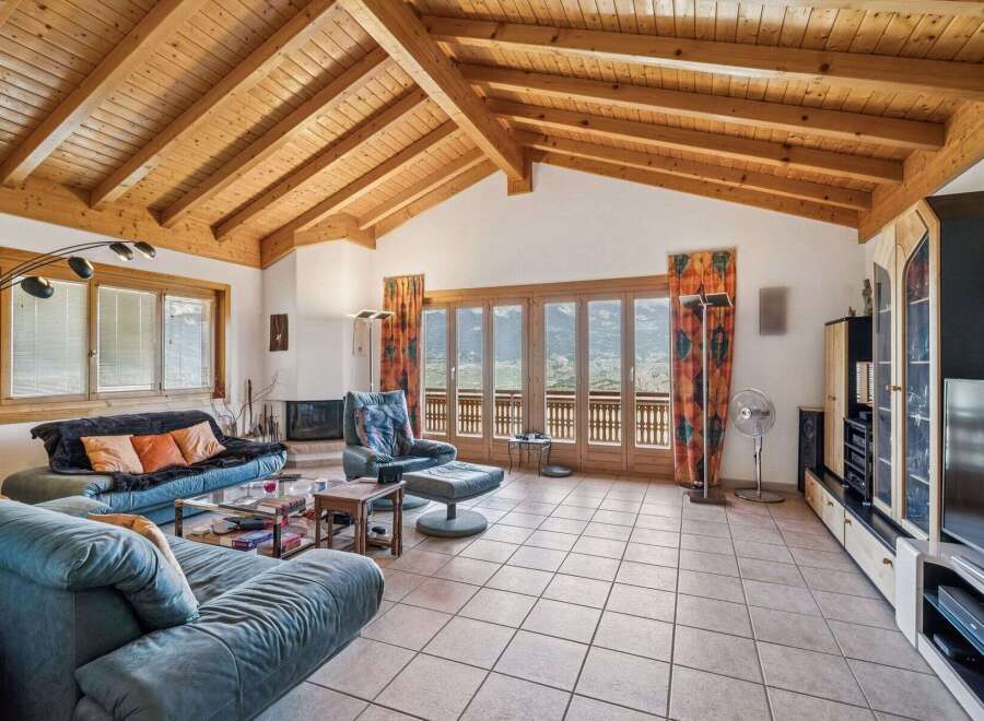 Experience breathtaking mountain views from this stunning living room, featuring a vaulted wood-beamed ceiling and expansive glass doors.