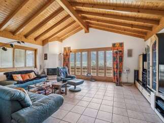 Experience breathtaking mountain views from this stunning living room, featuring a vaulted wood-beamed ceiling and expansive glass doors.