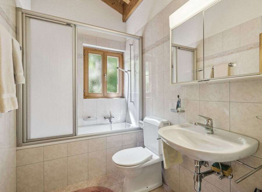 This charming bathroom features a bathtub with a sliding glass door, perfect for a relaxing soak.