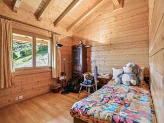 Experience cozy living in this charming wooden cabin bedroom, featuring a comfortable bed adorned with a vibrant floral comforter.