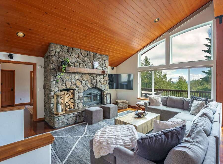Experience breathtaking mountain views from this stunning living room, featuring a magnificent stone fireplace and a vaulted wood-paneled ceiling.