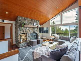 Experience breathtaking mountain views from this stunning living room, featuring a magnificent stone fireplace and a vaulted wood-paneled ceiling.