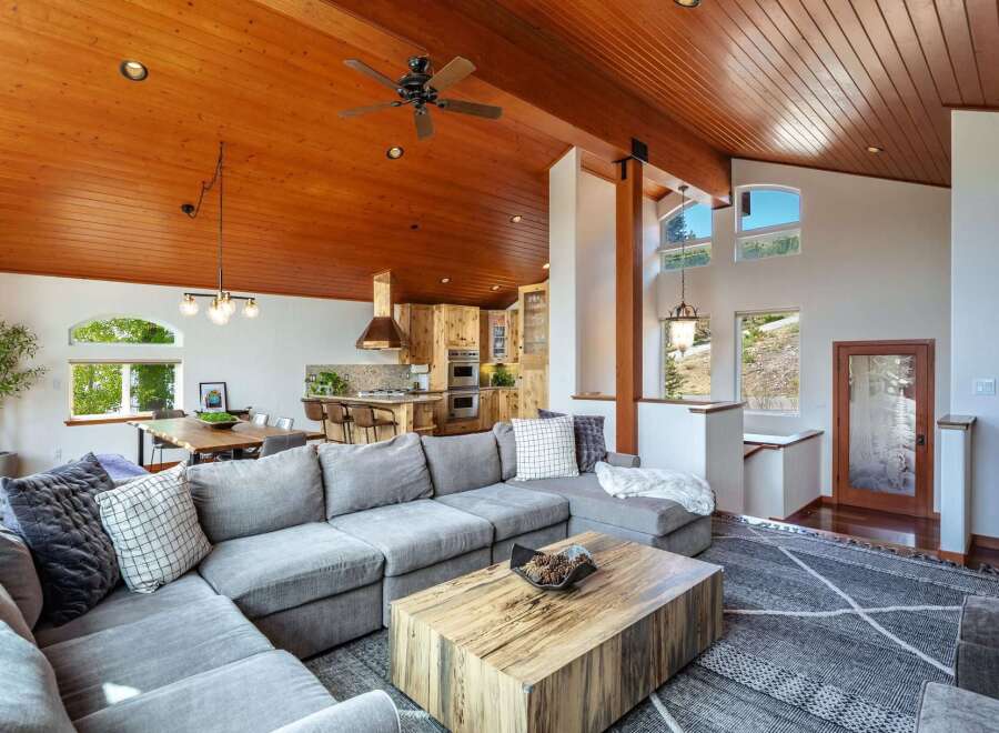 Experience rustic charm and modern comfort in this stunning open-concept living space, featuring a soaring wood-paneled ceiling and a cozy sectional sofa perfect for gatherings.