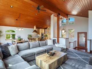 Experience rustic charm and modern comfort in this stunning open-concept living space, featuring a soaring wood-paneled ceiling and a cozy sectional sofa perfect for gatherings.