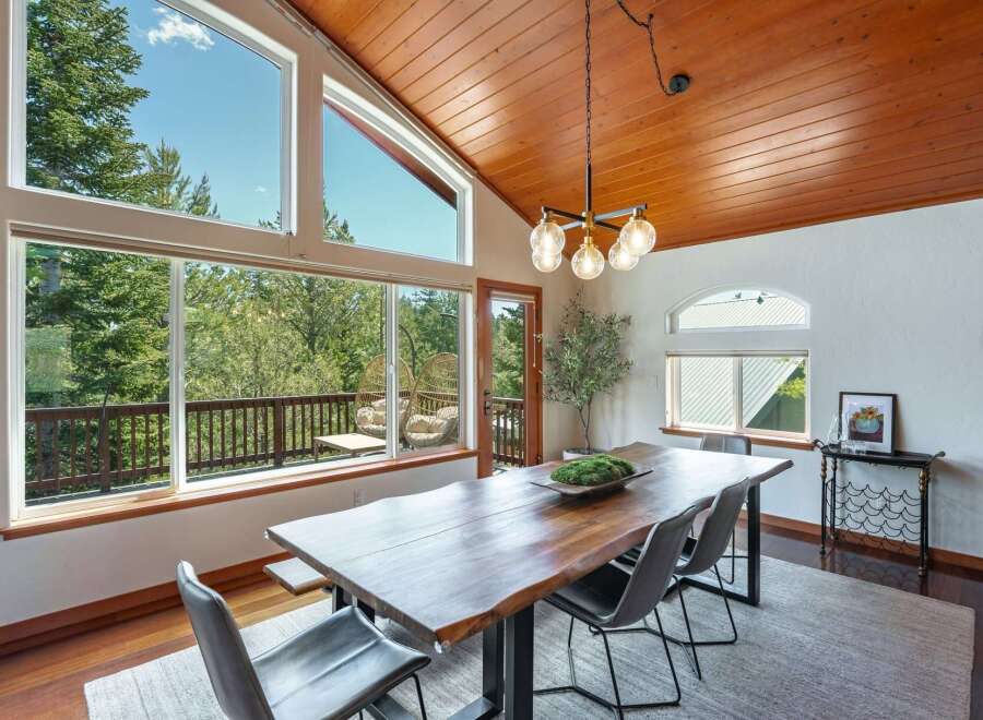 Experience breathtaking views from this stunning dining room, featuring a live-edge wood table and large windows that open to a private balcony surrounded by lush trees.