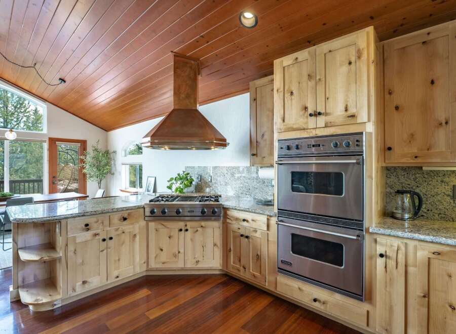 Experience rustic charm and modern convenience in this stunning kitchen, featuring a vaulted wood-paneled ceiling and a striking copper range hood.