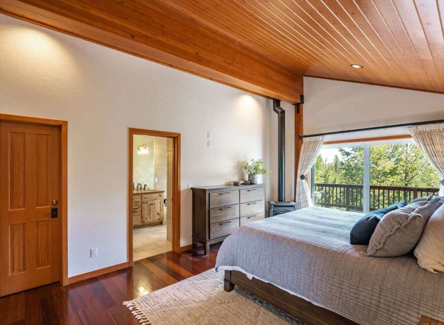 Experience serene living in this charming bedroom featuring a cozy wood-burning stove and a private balcony with breathtaking forest views.