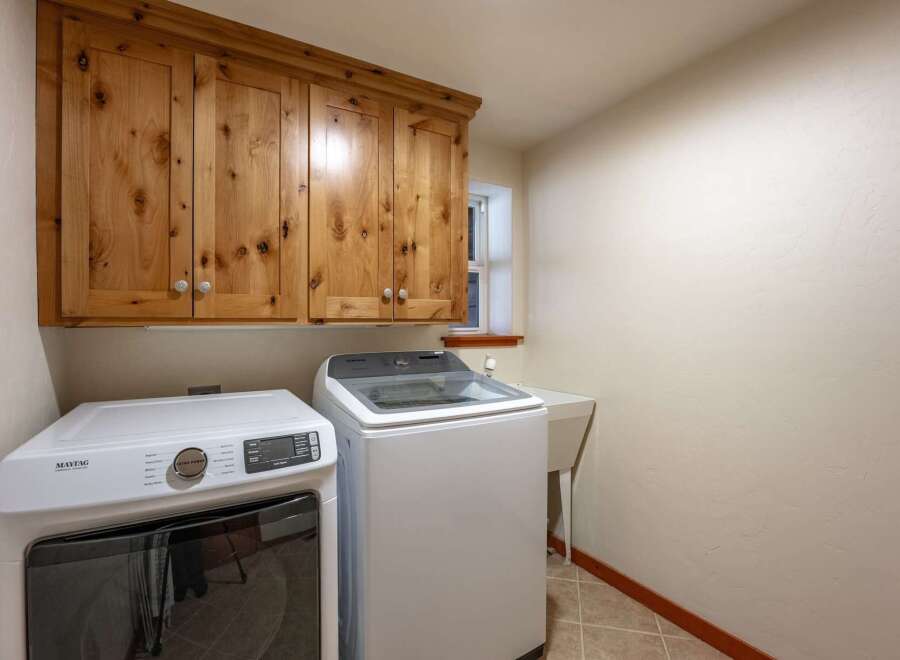 This laundry room features ample storage with beautiful knotty pine cabinets above the washer and dryer.