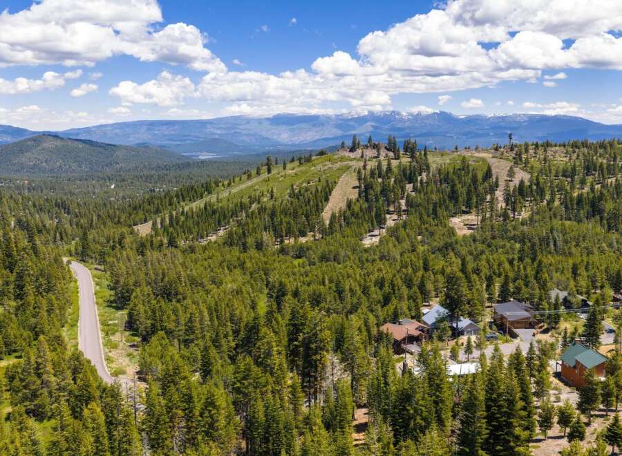 Discover your dream mountain retreat nestled amidst a lush pine forest, offering breathtaking panoramic views of snow-capped peaks and a serene lake.