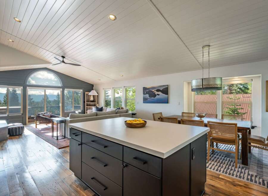 Experience breathtaking mountain views from this stunning open-concept living space, featuring a vaulted ceiling with exposed beams and a large arched window.