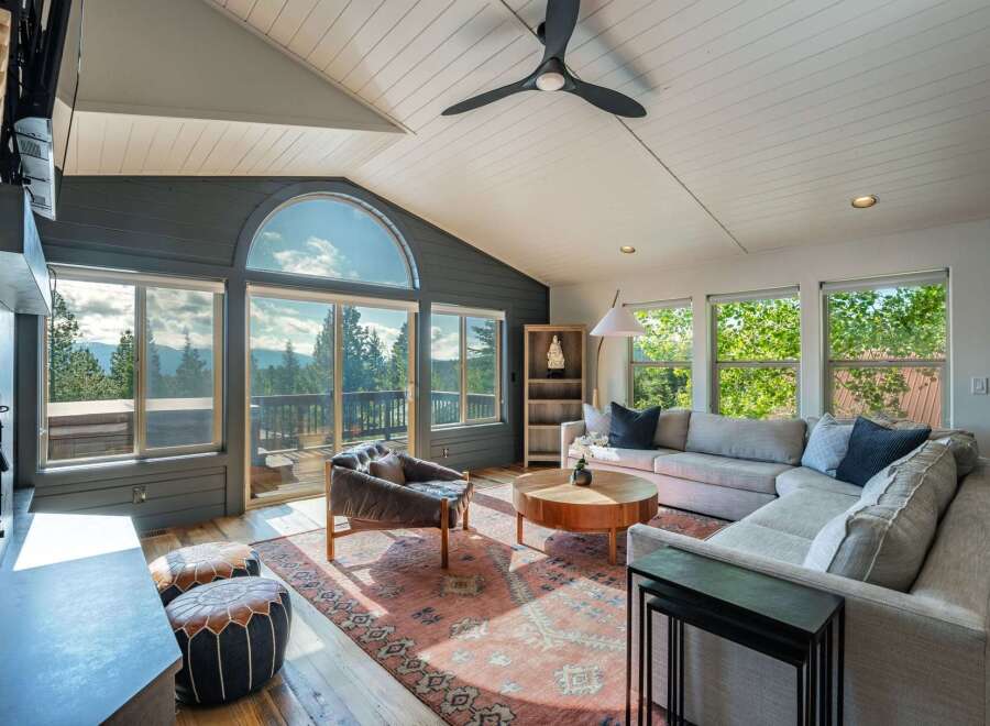 Experience breathtaking mountain views from this stunning living room, featuring a grand arched window and expansive glass doors that open to a scenic deck.