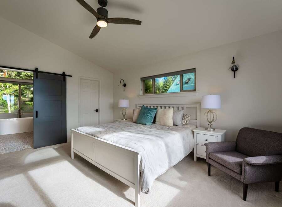 Experience luxury and tranquility in this stunning bedroom featuring a spacious white bed, elegant bedside tables with lamps, and a comfortable armchair.