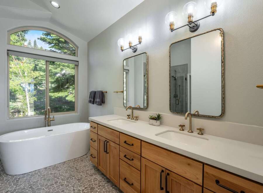 Experience luxury in this stunning bathroom featuring a freestanding soaking tub with a picturesque arched window view of lush greenery.