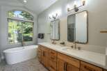 Experience luxury in this stunning bathroom featuring a freestanding soaking tub with a picturesque arched window view of lush greenery.