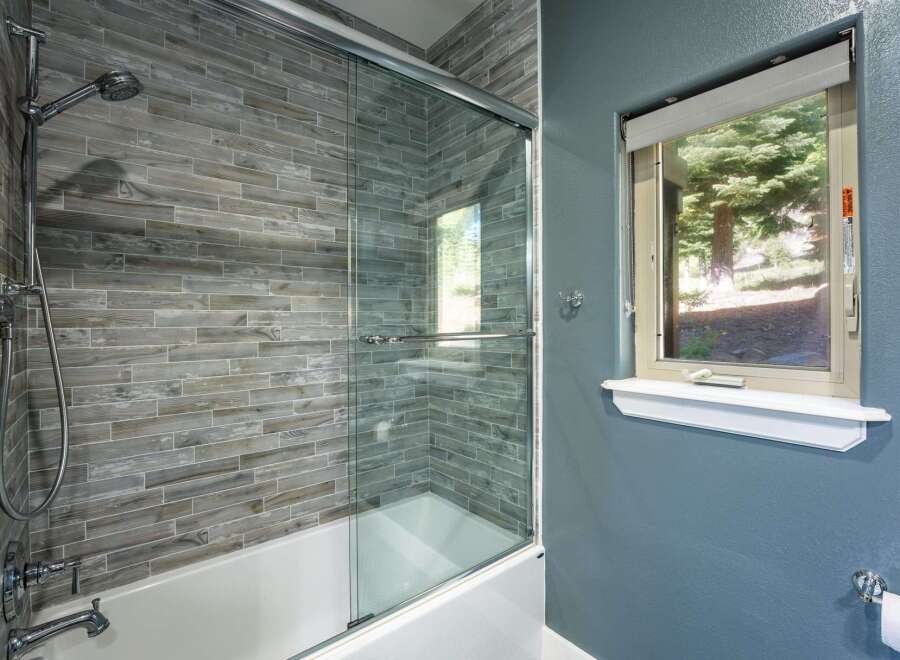 Experience modern comfort in this bathroom featuring a sleek glass shower enclosure over a pristine white bathtub.