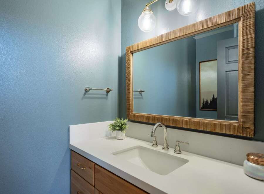 This modern bathroom features a sleek vanity with a white countertop and a undermount sink, complemented by a large, natural wood-framed mirror.