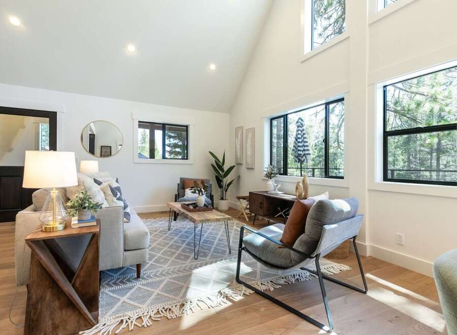 This living room boasts a vaulted ceiling and large windows that flood the space with natural light, offering serene forest views.