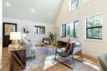 This living room boasts a vaulted ceiling and large windows that flood the space with natural light, offering serene forest views.
