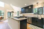 Experience modern living in this stunning kitchen featuring sleek dark cabinetry and a spacious island with a built-in gas range.