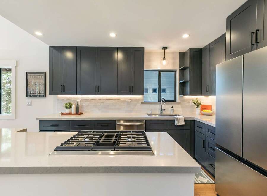 Experience modern luxury in this stunning kitchen, featuring sleek dark cabinetry, a spacious quartz island with a built-in gas range, and elegant subway tile backsplash.